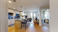 This contemporary residence in Denver, CO offers a well-designed open-concept layout that seamlessly connects the kitchen, dining, and living areas. The kitchen is appointed with light wood cabinetry extending to the ceiling, stainless steel appliances including a side-by-side refrigerator, a blue subway tile backsplash, stone countertops, and a central island with bar seating illuminated by pendant lighting. Light hardwood flooring flows throughout the main living areas, enhancing the bright, airy atmosphere created by large windows and clean white walls. The living room opens directly to a private balcony through floor-to-ceiling windows, offering expansive views of the Denver skyline and surrounding mountains. The primary bedroom is a generous retreat featuring a sliding-door closet and direct access to an en suite bathroom complete with a walk-in closet, wood-toned vanity with stone countertop, and a tiled shower. The second bathroom includes a soaking tub with a tiled surround, a wood-framed vanity, and warm hardwood flooring. The three additional bedrooms are comfortably proportioned with ample closet space. The unit's modern, neutral palette and quality finishes throughout create a cohesive and functional living environment.