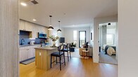 This contemporary residence in Denver, CO offers a well-designed open-concept layout that seamlessly connects the kitchen, dining, and living areas. The kitchen is appointed with light wood cabinetry extending to the ceiling, stainless steel appliances including a side-by-side refrigerator, a blue subway tile backsplash, stone countertops, and a central island with bar seating illuminated by pendant lighting. Light hardwood flooring flows throughout the main living areas, enhancing the bright, airy atmosphere created by large windows and clean white walls. The living room opens directly to a private balcony through floor-to-ceiling windows, offering expansive views of the Denver skyline and surrounding mountains. The primary bedroom is a generous retreat featuring a sliding-door closet and direct access to an en suite bathroom complete with a walk-in closet, wood-toned vanity with stone countertop, and a tiled shower. The second bathroom includes a soaking tub with a tiled surround, a wood-framed vanity, and warm hardwood flooring. The three additional bedrooms are comfortably proportioned with ample closet space. The unit's modern, neutral palette and quality finishes throughout create a cohesive and functional living environment.