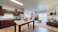 This well-appointed 2-bedroom, 2-bathroom residence in Rochester, MN offers a thoughtfully designed single-level layout that maximizes functionality and comfort. The open-concept kitchen and living area serves as the heart of the home, where rich dark-walnut cabinetry, granite countertops, a classic white subway tile backsplash, and a full suite of stainless steel appliances create a polished, modern kitchen. A central island with a granite surface provides additional workspace and casual dining. Warm hardwood-style flooring flows throughout the main living areas, transitioning seamlessly into the carpeted living room, which is bathed in natural light from a large sliding glass door that opens to an outdoor balcony or patio. Both bedrooms are comfortably scaled, featuring plush carpeting, natural light from wide windows with outdoor views, and access to dedicated closets. The two bathrooms are finished with matching dark cabinetry and granite vanities, with hardwood-style flooring adding continuity. One bathroom conveniently connects to an in-unit laundry area with a stacked washer and dryer. Three closets throughout the unit ensure ample storage. The neutral color palette and clean finishes give the space a bright, move-in-ready feel.