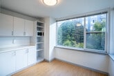 Located on the third floor of 1815 Bellevue Ave in Seattle's Capitol Hill neighborhood, Unit 311 is a thoughtfully designed single-floor residence that balances clean, modern aesthetics with practical functionality. The main living area is finished with warm bamboo-style hardwood flooring that runs throughout, creating a cohesive and inviting atmosphere. Large corner windows flood the space with natural light while framing views of the surrounding mature tree canopy, bringing a sense of the outdoors inside. Built-in white cabinetry lines one wall, offering generous storage alongside open shelving and an integrated microwave — ideal for efficient everyday living. The layout flows naturally toward the entryway, which features a bold accent door adding a pop of color to the otherwise clean, neutral palette. The bathroom is well-appointed with a modern floating vanity, a large mirror, a walk-in shower, and a separate toilet area, all finished with bright white walls and resilient flooring. Accessibility features, including grab bars, are also present. The unit's design is characterized by its crisp white walls, efficient use of space, and abundant natural light, offering a comfortable and contemporary living environment in the heart of Seattle.