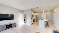 Located at 4500 E Third St in Bloomington, Indiana, this modern single-floor unit offers 2 bedrooms and 3 bathrooms within a thoughtfully designed, contemporary layout. Light-toned luxury vinyl plank flooring and neutral gray walls flow consistently throughout, creating a clean, cohesive aesthetic.

The open-concept living and kitchen area forms the heart of the unit. The kitchen is outfitted with white shaker-style cabinetry, stainless steel appliances including a refrigerator, range, and microwave, and a central island with a white quartz countertop, undermount sink, and pendant lighting above. A dedicated in-unit laundry room with a full-size Whirlpool washer and dryer adds everyday convenience.

The living room is bright and airy, with recessed lighting and a glass sliding door that opens to a private balcony overlooking a green outdoor area. The primary bedroom features large, dark-framed windows on multiple walls that invite abundant natural light and exterior views. The second bedroom also includes a ceiling fan, a sizable window, and space for a desk, making it functional as a sleeping or study room. Three well-appointed bathrooms feature light-toned finishes, white vanities, and brushed nickel hardware. A dedicated closet completes this efficiently planned, modern living space.