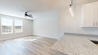 This well-designed 1-bedroom, 1-bathroom residence offers a thoughtful, open-concept layout across a single floor. The combined kitchen and living area serves as the heart of the home, showcasing crisp white shaker cabinetry, granite countertops, and a full suite of stainless steel appliances including a range, microwave, dishwasher, and refrigerator. A peninsula with additional storage provides casual dining or prep space, while a stylish pendant light fixture above and recessed lighting throughout keep the area bright and inviting. Light-toned hardwood-style flooring extends across the main living areas, complemented by large windows that allow natural light to fill the space. A ceiling fan in the living area adds both function and style. The bedroom features plush carpet flooring, dual windows with natural light, a ceiling fan, and direct access to a spacious walk-in closet equipped with wire shelving for organized storage. The full bathroom is appointed with a granite-topped vanity, white cabinetry, a large mirror, and a tub-shower combination with clean white tile surround. An entry closet near the front door offers additional convenient storage. The overall aesthetic is clean, contemporary, and move-in ready.