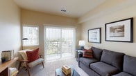 This single-floor residence offers a thoughtfully designed layout across two bedrooms and two bathrooms, combining comfortable living spaces with practical finishes throughout. The living room serves as the heart of the home, featuring plush carpeting, warm neutral walls, and generous natural light supplied by a large sliding glass door that opens onto a private balcony with open outdoor views. Vertical blinds provide flexible light control, and the space easily accommodates a full seating arrangement.

The kitchen is well-equipped, featuring rich dark wood cabinetry, gray countertops, a double-basin sink, and wood-look flooring. A peninsular counter connects the kitchen to the living area, creating an open, functional flow ideal for everyday use.

Both bedrooms are carpeted and filled with natural light from large windows fitted with vertical blinds. Each room offers comfortable proportions suitable for a full bedroom setup. One bathroom includes a full tub-shower combination with wood-look flooring, while the second bathroom features a wood vanity with integrated sink, a large mirror, and matching wood-look flooring. The overall ambiance is warm, neutral, and move-in ready.