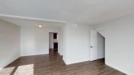 Located at 200 Seven Oaks Rd in Durham, North Carolina, this two-story home offers a clean and functional layout designed for comfortable everyday living. The interior showcases dark hardwood-style flooring that runs throughout the main level, providing a warm contrast against the bright white walls and crisp trim work. The main living area is open and airy, benefiting from natural light that highlights the neutral color palette and textured ceiling finish. A staircase is conveniently positioned off the main living space, providing access to the second floor. The layout flows naturally from the living area toward additional rooms, with a glimpse of a kitchen visible in the background, featuring dark cabinetry that adds depth and character to the space. Interior doors with classic paneled designs are found throughout, contributing to a tidy, cohesive aesthetic. Overhead lighting fixtures provide consistent illumination, and ceiling vents suggest a central HVAC system for year-round comfort. The overall ambiance of the home is fresh and move-in ready, with a neutral design that offers a versatile canvas for a variety of interior styles and furnishings.