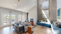 Located at 3594 Mt Diablo Blvd in Lafayette, CA, this thoughtfully designed single-floor space offers a compelling blend of modern aesthetics and functional layout. The living room serves as the centerpiece, boasting dramatic vaulted ceilings that lend an airy, expansive feel. A bold geometric-patterned feature wall rises to full height, flanking a sleek built-in fireplace that anchors the room. Light wood flooring runs throughout, complementing the soft, neutral furnishings and warm walnut accents. French doors open to an outdoor area, flooding the space with natural light. A cozy built-in bench with teal upholstery offers an additional seating nook. The kitchen is outfitted with walnut-toned cabinetry, white quartz countertops, open wood shelving, a stainless steel sink, and stainless steel appliances including a compact refrigerator and oven — combining style with practicality. Textured wallcovering adds depth and character to the kitchen's backdrop. The bathroom features large-format tile wainscoting, a wood-toned vanity with a white countertop, and accessibility-ready grab bars, reflecting thoughtful, inclusive design. Recessed lighting throughout ensures a clean, polished finish across all areas of the space.