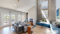 Located at 3594 Mt Diablo Blvd in Lafayette, CA, this thoughtfully designed single-floor space offers a compelling blend of modern aesthetics and functional layout. The living room serves as the centerpiece, boasting dramatic vaulted ceilings that lend an airy, expansive feel. A bold geometric-patterned feature wall rises to full height, flanking a sleek built-in fireplace that anchors the room. Light wood flooring runs throughout, complementing the soft, neutral furnishings and warm walnut accents. French doors open to an outdoor area, flooding the space with natural light. A cozy built-in bench with teal upholstery offers an additional seating nook. The kitchen is outfitted with walnut-toned cabinetry, white quartz countertops, open wood shelving, a stainless steel sink, and stainless steel appliances including a compact refrigerator and oven — combining style with practicality. Textured wallcovering adds depth and character to the kitchen's backdrop. The bathroom features large-format tile wainscoting, a wood-toned vanity with a white countertop, and accessibility-ready grab bars, reflecting thoughtful, inclusive design. Recessed lighting throughout ensures a clean, polished finish across all areas of the space.