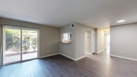 Located at 441 Manor Rd in Newport News, VA, this 2-bedroom, 1-bathroom single-floor home offers a practical and well-organized layout. The combined living and dining area is anchored by dark hardwood-style flooring and features a sliding glass door that floods the space with natural light and provides direct outdoor access. A pass-through window with a granite-style countertop connects the living area to the kitchen, creating an open, communicative flow between spaces. The kitchen is equipped with slate-gray cabinetry, dark granite-style countertops, matching appliances including a dishwasher, and a window above the sink that brings in additional natural light. Light wood-style flooring completes the kitchen's clean, modern aesthetic. The dining area features the same pass-through design, making it ideal for casual entertaining. Both bedrooms are carpeted for comfort, with neutral wall tones and ample natural light from multiple windows. The primary bedroom includes a dedicated closet, while the secondary bedroom benefits from dual corner windows. The full bathroom is appointed with dark navy cabinetry, a white countertop vanity, and contemporary lighting. Additional functional spaces include a laundry area, utility room, hallway, and two closets, ensuring excellent storage throughout.