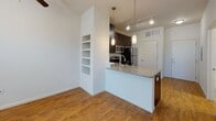 Located in Mount Pleasant, South Carolina, this single-story residence offers a well-organized layout with functional design throughout. The kitchen serves as a central feature, showcasing dark espresso cabinetry that extends to the upper walls, granite countertops, and a full suite of stainless steel appliances including a range, built-in microwave, and refrigerator. A peninsula with a granite surface and undermount sink separates the kitchen from the living area, creating an open, connected flow. Track lighting and pendant fixtures illuminate the space effectively. Adjacent to the kitchen, a built-in shelving unit provides convenient display or storage space. The living area is finished with warm hardwood-style flooring that continues throughout the unit, contributing to a cohesive aesthetic. The bedroom offers natural light through multiple windows fitted with blinds, complemented by a ceiling fan. A doorway leads to what appears to be a walk-in closet. The bathroom features neutral tile flooring, a soaking tub with tiled surround, a dark vanity with granite countertop, and brushed nickel fixtures and grab bar accents. Neutral wall tones and consistent finishes throughout create a clean, modern ambiance.