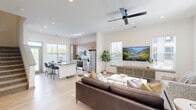 This two-story home offers a well-designed layout across two floors, with the majority of the living space situated on the main level. The open-concept ground floor features light hardwood-style flooring, recessed lighting, and an abundance of natural light from multiple windows. The living area is generously proportioned, accommodating a ceiling fan and large windows that fill the space with daylight. It flows seamlessly into the kitchen, which is equipped with stainless steel appliances, warm taupe cabinetry, a central island featuring a gray quartz countertop with an integrated sink, and bar seating — ideal for both cooking and entertaining.

A carpeted staircase leads to the upper floor, which houses the two bedrooms, a dedicated office, and additional bathrooms. The primary bedroom includes a double-door closet and soft carpet flooring. The office is a bright, functional space with a distinctive green accent wall and a large window. The bathrooms are clean and modern, with one featuring a full tub-shower combination. Throughout the home, a neutral color palette, gray-paneled doors, and consistent finishes create a cohesive and contemporary aesthetic.