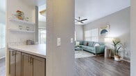 This thoughtfully designed single-floor residence offers a cohesive blend of modern finishes and comfortable living spaces. The open-concept living area features warm hardwood-style flooring, a ceiling fan, and generous natural light streaming through large windows with white blinds, creating a bright and welcoming atmosphere. The adjacent kitchen is well-equipped with stainless steel appliances — including a refrigerator, range, microwave, and dishwasher — complemented by gray shaker-style cabinetry, white quartz countertops, and a classic subway tile backsplash. A dedicated dining nook with a window provides a pleasant space for everyday meals. The primary bedroom offers plush carpeting, ample natural light, and access to a private en-suite bathroom featuring a wide vanity with quartz countertops, subway tile accents, gray cabinetry, and a walk-in closet visible in the mirror. A second bedroom provides a cozy retreat with carpet flooring and natural light. A versatile flex room, currently configured as a home office, features carpeting, a large window, and vaulted ceiling lines. The second full bathroom includes a tub-shower combination, a single vanity with modern fixtures, and hardwood-style flooring, maintaining the home's consistent, refined aesthetic throughout.