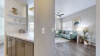 This thoughtfully designed single-floor residence offers a cohesive blend of modern finishes and comfortable living spaces. The open-concept living area features warm hardwood-style flooring, a ceiling fan, and generous natural light streaming through large windows with white blinds, creating a bright and welcoming atmosphere. The adjacent kitchen is well-equipped with stainless steel appliances — including a refrigerator, range, microwave, and dishwasher — complemented by gray shaker-style cabinetry, white quartz countertops, and a classic subway tile backsplash. A dedicated dining nook with a window provides a pleasant space for everyday meals. The primary bedroom offers plush carpeting, ample natural light, and access to a private en-suite bathroom featuring a wide vanity with quartz countertops, subway tile accents, gray cabinetry, and a walk-in closet visible in the mirror. A second bedroom provides a cozy retreat with carpet flooring and natural light. A versatile flex room, currently configured as a home office, features carpeting, a large window, and vaulted ceiling lines. The second full bathroom includes a tub-shower combination, a single vanity with modern fixtures, and hardwood-style flooring, maintaining the home's consistent, refined aesthetic throughout.