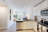 Located at 120 N Compass Way in Dania Beach, FL, this contemporary one-bedroom, one-bathroom residence offers a thoughtfully designed open-concept floor plan. Light wood-look tile flooring flows throughout the main living areas, enhancing the bright and airy atmosphere created by crisp white walls and abundant natural light.

The kitchen is a standout feature, outfitted with sleek white cabinetry, grey quartz countertops, a subway tile backsplash, and a full suite of stainless steel appliances including a refrigerator, range, microwave, and dishwasher. A peninsula with bar seating connects the kitchen seamlessly to the living area, making it ideal for both everyday living and entertaining.

The living room is bathed in natural light from floor-to-ceiling sliding glass doors that open to a private balcony, offering views of the surrounding community and palm-lined surroundings. A ceiling fan adds comfort to the space.

The bedroom is a comfortable retreat with plush carpeting, a ceiling fan, a large window with outdoor views, and a closet with sliding doors. The bathroom features a spacious glass-enclosed walk-in shower with white tile surround, mosaic tile flooring, and matte black fixtures, conveying a clean, modern aesthetic throughout.