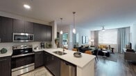 Located at 3400 E Southern Ave in Phoenix, AZ, this single-floor residential unit offers a thoughtfully designed open-concept layout that seamlessly connects the kitchen, dining, and living areas. The kitchen is a standout feature, equipped with dark wood cabinetry, stainless steel appliances including a range, microwave, dishwasher, and refrigerator, complemented by a large center island with a double-basin sink and white quartz countertops. Stylish pendant lighting adds a modern touch above the island. Wood-style flooring flows throughout the main living areas, contributing to a warm and cohesive aesthetic. The living room is bright and inviting, featuring a ceiling fan, large windows with blinds that allow ample natural light, and enough space for a full seating and dining arrangement. The primary bedroom features a distinctive green accent wall, ceiling fan, and a window with drape treatments, creating a serene retreat. A second bedroom provides a cozy space accented with southwestern-inspired artwork. The bathroom is generously proportioned, offering a single-sink vanity with dark cabinetry, a soaking tub with shower, wood-style flooring, and direct access to a spacious walk-in closet. The unit entry opens directly into the kitchen area, providing a clean and functional flow throughout the home.