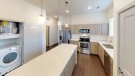 This single-floor unit presents a thoughtfully designed layout with a contemporary aesthetic throughout. The kitchen serves as a standout feature, showcasing a generous island with a quartz countertop, light wood cabinetry, and a classic white subway tile backsplash. Stainless steel appliances — including a range, microwave, dishwasher, and refrigerator with an ice and water dispenser — complement the space, while pendant lighting adds a modern touch. Dark hardwood-style flooring runs through the kitchen and connects seamlessly to the adjacent areas.

The bedrooms are finished with soft, neutral carpet and ceiling fans, contributing to a comfortable and quiet atmosphere. One bedroom benefits from a large window overlooking a brick exterior, allowing natural light to fill the room. The primary bedroom is notable for its access to a walk-in closet and an en-suite bathroom, providing a sense of privacy and functionality.

The bathroom features wood-toned cabinetry with a white quartz vanity top, a large mirror with modern vanity lighting, and a soaking tub enclosed by white subway tile. Dark hardwood-style flooring ties the space together. Overall, the unit presents a clean, modern finish with consistent design elements across all rooms, creating a cohesive and inviting living environment.