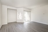 This thoughtfully designed 1-bedroom, 1-bathroom unit offers a clean, modern aesthetic throughout its single-floor layout. The living area is bright and open, featuring light-toned luxury vinyl plank flooring, neutral walls, and a textured ceiling. A large sliding glass door paired with an adjacent window floods the space with natural light and provides direct access to a private balcony with outdoor views, creating an airy and welcoming atmosphere.

The kitchen is a standout feature, outfitted with white shaker-style cabinetry, gleaming quartz countertops, a peninsula with an undermount sink and matte black faucet, and a full suite of stainless steel appliances including a refrigerator, range, and over-the-range microwave. The kitchen opens conveniently to the laundry area, which accommodates a side-by-side washer and dryer.

The bedroom offers a comfortable footprint with the same warm vinyl plank flooring and neutral tones found throughout the unit, providing a calm and restful environment. The full bathroom is clean and functional, featuring a soaking tub with a tiled surround, toilet, and matte black hardware accents. The entrance provides a practical transition into the living space, completing this efficient and modern single-level layout.