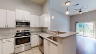 This single-story, one-bedroom, one-bathroom residence offers a thoughtfully designed layout that maximizes functionality and comfort. The combined kitchen and living area serves as the heart of the home, featuring warm wood-look flooring, high ceilings that enhance the sense of openness, and a sliding glass door that fills the space with natural light while providing direct access to an outdoor area with greenery views.

The kitchen is well-equipped with a full suite of stainless steel appliances, including a refrigerator, electric range, microwave, and dishwasher. Crisp white cabinetry provides ample storage, while granite-patterned countertops extend into a peninsula with an integrated sink — an ideal space for casual dining or meal prep. Stylish pendant lighting accents the peninsula area.

The bedroom is carpeted for comfort and benefits from a large window with outdoor views, including glimpses of a pool area. Tall ceilings continue throughout, adding an airy feel. A dedicated closet provides convenient storage adjacent to the bedroom.

The bathroom is finished with a warm wood-toned vanity topped with a granite-look countertop and an undermount sink, complemented by a large framed mirror. A full tub-shower combination and light tile flooring complete the space. The overall palette of neutral grays and whites throughout creates a clean, cohesive aesthetic.