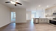 This well-appointed single-story home in Clarksville, Tennessee offers a thoughtfully designed open-concept layout across two bedrooms, three bathrooms, and a dedicated laundry room. The main living area flows seamlessly from the living room into the kitchen, where a central island with a built-in sink and stainless steel dishwasher serves as the focal point. The kitchen is outfitted with gray shaker-style cabinetry, a tile backsplash, white quartz countertops, stainless steel appliances including a refrigerator, range, and microwave, and pendant lighting that adds a modern touch. Recessed lighting and a ceiling fan enhance the open living area, while natural light filters in through the windows and glass-paneled back door. The primary bedroom is generously sized, featuring a ceiling fan, hardwood-style flooring, and access to a private en-suite bathroom complete with a dual-sink vanity, soaking tub, and walk-in closet. The second bedroom is carpeted, naturally lit, and includes its own ceiling fan and closet access. The dedicated laundry room houses a full-size washer and dryer with overhead shelving for added storage. Consistent hardwood-style flooring flows throughout the main areas, tying together this clean, modern home.