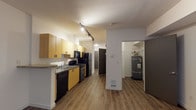 Located on the third floor at 2201 4th Avenue in Seattle's vibrant Belltown neighborhood, Unit 306 is a thoughtfully designed single-floor residence finished with warm wood-tone luxury vinyl plank flooring throughout. The kitchen is efficiently laid out along one wall, featuring light maple cabinetry, granite-style countertops with a breakfast bar overhang, a double sink, and a full suite of black appliances including a refrigerator, range, dishwasher, and built-in microwave. Track lighting illuminates the kitchen and hallway, adding a modern touch. The open living area is bright and airy, anchored by a large multi-pane window that invites natural light and offers views of the surrounding urban streetscape. The space includes a dedicated utility closet housing a water heater, providing convenient in-unit infrastructure. The bathroom is clean and well-appointed, featuring a wood-tone vanity with ample cabinet storage, a large wall mirror with overhead lighting, and a full-width countertop with an integrated sink. Neutral white walls and consistent flooring throughout the unit create a cohesive, move-in-ready atmosphere suited for urban living in the heart of Seattle.