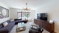 This single-floor residence showcases a thoughtfully designed open-concept layout that seamlessly connects the kitchen and living areas. The kitchen is a standout feature, outfitted with rich dark-wood cabinetry, stainless steel appliances including a gas range, over-the-range microwave, and French door refrigerator. Light-toned granite countertops and a subway tile backsplash add refined detail, while light hardwood flooring runs throughout the main living spaces, creating a warm, cohesive aesthetic. Recessed linear ceiling lighting enhances the kitchen's modern feel.

The living area is generously proportioned and bathed in natural light through large floor-to-ceiling windows that offer views of the surrounding streetscape. A striking multi-globe brass chandelier serves as a focal point, complementing the contemporary character of the space.

The bedroom is a serene and comfortable retreat, featuring plush carpeting, a sliding closet, and a window that brings in natural light. Its neutral palette and clean lines create a calm, restful atmosphere.

The bathroom maintains the same refined design language, featuring a dark-wood vanity with granite countertops, a large mirror, tile flooring, and a tiled walk-in shower, all presented in a crisp, bright finish. This residence offers a polished and cohesive living experience with modern finishes at every turn.