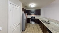 Located at 820 W Fifth St in the heart of uptown Charlotte, NC, this single-floor residence offers a well-designed, open-concept layout that balances modern finishes with comfortable living spaces. The kitchen serves as a focal point, featuring rich dark espresso cabinetry, stainless steel appliances including a refrigerator, range, and over-the-range microwave, granite countertops, a tile backsplash, and wood-look flooring. A peninsula with a granite overhang connects the kitchen to the living area, creating a seamless flow ideal for entertaining. The living space is finished with neutral-toned carpet and benefits from natural light. The bedroom is a generously sized, carpeted retreat with a ceiling fan, a large window, and French doors that open to an outdoor area, allowing for ample natural light and ventilation. A walk-in closet with wire shelving provides practical storage. The bathroom is finished with wood-look flooring, a dark-framed vanity mirror, granite countertops, and dark cabinetry, with direct access to the walk-in closet. Throughout the space, a neutral color palette of warm beige and greige tones creates a cohesive and inviting ambiance.