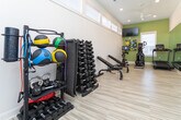 Located at 129 NC-801 S in Bermuda Run, NC, this fitness center is a well-appointed, single-level space designed to support a full range of workout activities. The room features light wood-look flooring that runs throughout, contributing to a clean and airy aesthetic. High ceilings with recessed lighting and a ceiling fan enhance the sense of openness, while a row of clerestory windows along the upper walls floods the space with abundant natural light without sacrificing wall space needed for equipment.

A floor-to-ceiling mirror spans one full wall, visually expanding the room and providing functional feedback during exercise. Multiple flat-screen televisions are mounted at strategic angles, ensuring visibility from various workout stations. The accent walls are painted in a soft sage green, adding a subtle, energizing pop of color against the predominantly white walls and trim.

The fitness center is equipped with treadmills, elliptical trainers, and stationary bikes, several of which feature integrated digital displays. A dedicated free weight area includes an adjustable dumbbell rack and adjustable benches, supporting strength training. Colorful artwork adds a finishing decorative touch, creating an inviting, motivating environment well-suited for a community fitness facility.