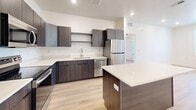 Located at 2427 Quincy Ave in Ogden, Utah, this modern 2-bedroom, 2-bathroom residence offers a well-designed single-floor layout with contemporary finishes throughout. The open-concept living area seamlessly connects the kitchen, dining, and living spaces, creating a bright and functional environment. Light wood-look flooring runs throughout the unit, complementing the clean white walls and recessed lighting.

The kitchen is a standout feature, equipped with dark wood cabinetry, white quartz countertops, a large center island, and a full suite of stainless steel appliances including a refrigerator, dishwasher, range, and microwave. A stylish glass-paneled door leads to the private balcony, extending the living space outdoors.

Both bedrooms are well-proportioned and filled with natural light from large windows with views of surrounding greenery. Each room features the same warm wood flooring and clean, neutral palette. The primary bedroom includes an en-suite bathroom and a dedicated walk-in closet with built-in shelving. The second bathroom offers a full tub-shower combo, dark wood vanity, white quartz countertop, and a large mirror. A dedicated laundry area and hallway with two closets round out this thoughtfully designed residence.