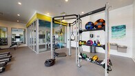 Located at 1105 E Twiggs St in the heart of Tampa, Florida, this single-floor fitness center is thoughtfully designed to support a wide range of workout routines. The space is organized into distinct functional zones, each tailored to a specific type of training. The main workout area features a multi-station functional training rig complete with TRX suspension straps, gymnastic rings, and battle ropes, alongside a comprehensive rack of medicine balls, kettlebells, and slam balls. A dedicated cardio zone lines the perimeter, outfitted with multiple treadmills, elliptical trainers, stair climbers, and a rowing machine, all positioned beneath large windows that flood the space with natural light. Bold olive-yellow accent walls and a durable concrete-finish floor give the gym a modern, energetic aesthetic, while ceiling fans maintain air circulation throughout. A separate spin studio with a vibrant teal ceiling houses indoor cycling bikes, wall-mounted TVs, and full-length mirrors, creating an immersive group fitness environment. The free weights area includes a dumbbell rack and an adjustable bench, complemented by mirrors and a mounted flat-screen TV. Glass-panel walls connect the zones visually, enhancing the open feel of the overall facility.