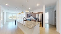 This well-appointed single-floor residence offers a thoughtfully designed open-concept layout that seamlessly connects the living, dining, and kitchen areas. The kitchen serves as the centerpiece of the space, showcasing an expansive granite-topped island with seating, warm wood-tone cabinetry, white subway tile backsplash, and a full suite of stainless steel appliances including a refrigerator, range, and built-in microwave. Stylish pendant lights hang above the island, adding a contemporary touch. Light-toned hardwood-style flooring flows throughout the main living areas, enhancing the bright and airy atmosphere created by multiple windows with outdoor views.

A dedicated laundry area conveniently houses a full-size washer and dryer with additional shelving for storage. The bathrooms feature clean white tilework, a soaking tub with shower, granite vanity countertops, and light tile flooring laid in an elegant herringbone pattern. The bedrooms are finished with plush carpeting, ceiling fans, and generous natural light from large windows. Each bedroom is complemented by a spacious closet with double hanging rods and shelving, providing substantial storage. The living area opens to an exterior door, offering direct outdoor access and a welcoming sense of openness throughout.