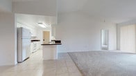 This well-designed single-floor residence offers a clean, bright aesthetic throughout, with white walls and an abundance of natural light creating an airy and welcoming atmosphere. The open-concept living area features a combination of light tile flooring and plush carpeting, seamlessly connecting the living space to the kitchen. A sliding glass door in the living room opens to a private balcony with outdoor views, while vaulted ceilings lend the space a generous sense of volume.

The kitchen is efficiently laid out in a galley style, featuring white cabinetry, rich dark granite countertops, white appliances including a range and built-in microwave, and a skylight that fills the space with natural light. A breakfast bar provides a convenient transition between the kitchen and living area, complemented by a separate dining nook with a pendant light fixture overhead.

The bedrooms are carpeted and generously sized, each with vertical blinds over large windows that allow for ample natural light and privacy. Closet space is provided in each room. The bathrooms are finished with tile flooring and dark granite vanity tops. The primary bathroom includes a standalone glass-enclosed shower, while the secondary bathroom features a full tub-and-shower combination, each maintaining the home's consistent, clean white palette.