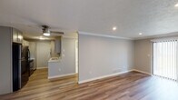 This single-floor unit offers a thoughtfully designed layout with a bright, open living area at its core. Warm-toned luxury vinyl plank flooring flows consistently throughout the space, complemented by soft grey walls, crisp white baseboards, and crown molding that frame each room with clean architectural detail. The living area is spacious and airy, equipped with a ceiling fan and recessed lighting, while a large sliding glass door fitted with vertical blinds floods the room with natural light. A front entryway provides a welcoming arrival point just off the main living space. The kitchen is efficiently arranged with grey shaker-style cabinetry, white countertops, a single-basin sink, and stainless steel appliances including a refrigerator, range, and microwave. A peninsula counter opens the kitchen toward the living area, enhancing the sense of connectivity. The bedroom is a comfortable retreat featuring a ceiling fan with light, a window with outdoor views, and the same consistent flooring found throughout. The bathroom is finished in a clean, modern palette with light tile flooring, a grey vanity with white countertop, a large mirror, and a tub-shower combination enclosed by a sliding glass door. Textured ceilings and recessed lighting add subtle character throughout this well-maintained and move-in ready space.