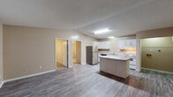 This single-floor unit offers a practical and well-organized layout designed for comfortable everyday living. The open-concept kitchen serves as the heart of the space, featuring white cabinetry, light speckled countertops, a double-basin stainless steel sink, a white electric range, a stainless steel refrigerator, and a dishwasher. A central kitchen island provides additional prep and storage space, while wood-look laminate flooring runs throughout the main living and kitchen areas, adding warmth and durability.

The bedrooms are carpeted for comfort and each includes a ceiling fan with integrated lighting. The primary bedroom offers direct access to an en-suite bathroom and features a built-in closet with organized shelving. Additional bedrooms are well-sized, with windows fitted with blinds that allow for natural light, and wall-mounted air conditioning units for climate control.

The bathrooms are clean and functional — the full bath includes a tub-shower combination, while a second bathroom provides a toilet, vanity, and towel bar. Textured ceilings are consistent throughout, and neutral warm-beige walls create a cohesive, understated ambiance across all rooms. The overall layout is efficient, making the most of the available space on a single level.