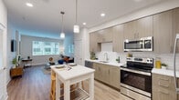 This thoughtfully designed one-bedroom, one-bathroom residence makes efficient use of its single-floor layout, offering a seamless blend of modern aesthetics and functional living. Light-toned hardwood flooring runs throughout, tying each space together cohesively.

The open-concept kitchen and living area forms the heart of the home. The kitchen features flat-front cabinetry in a warm wood tone, white subway tile backsplash, light quartz countertops, and a full suite of stainless steel appliances including a range, microwave, dishwasher, and refrigerator. Pendant lighting over a central island provides both task illumination and a casual dining option. The adjacent living area is bright and inviting, with a large window that draws in natural light.

The bedroom is a comfortable retreat, featuring a window with exterior views and draping curtains that allow for flexible light control. The bathroom is clean and modern, showcasing a glass-enclosed walk-in shower with white tile surround, a wood-toned vanity, and direct access to a dedicated closet equipped with built-in shelving and hanging rods — a practical storage solution that maximizes organization. The overall ambiance of the residence is contemporary, clean, and move-in ready.