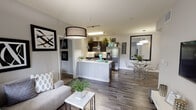 This well-appointed single-floor residence offers a thoughtfully designed open-concept layout that seamlessly connects the living, dining, and kitchen areas. The living room features rich wood-look flooring, a large window that invites natural light, and a stylish oversized pendant light fixture. A sectional sofa, accent wall art, and a wall-mounted television complete the space with a modern, coordinated aesthetic.

The kitchen is outfitted with dark cabinetry, stainless steel appliances including a side-by-side refrigerator, electric range, and built-in microwave, all set against clean white countertops. A peninsula provides additional prep space and serves as a natural transition to the dining area, which features a glass-top table and acrylic chairs beneath a pendant light.

Two bedrooms offer a comfortable retreat, each with plush carpet flooring, ceiling fans with integrated lighting, and windows with views of surrounding greenery. One bedroom includes a dedicated closet with built-in shelving, while the other features ample dresser space. The bathroom is finished with tile flooring, a large vanity mirror, white countertops, dark cabinetry, and a shower-tub combination, providing a clean and functional design.