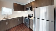 This single-floor, 2-bedroom, 2-bathroom residence offers a thoughtfully designed open-concept layout with a seamless flow between the living and kitchen areas. Rich, dark hardwood flooring extends throughout the main living spaces, creating a warm contrast against the bright white walls and ceilings. Large windows throughout the unit allow generous natural light to fill the space, with outdoor views adding to the airy atmosphere.

The kitchen is well-appointed with dark wood cabinetry, light countertops, a classic white subway tile backsplash, and a full suite of stainless steel appliances including a refrigerator, electric range, microwave, and dishwasher. A door from the living area provides access to an outdoor balcony area.

Both bedrooms feature plush carpeting, clean white walls, and windows that invite natural light and views of the surrounding neighborhood. One bedroom includes a spacious walk-in closet outfitted with wire shelving and hanging rods for ample storage.

The bathrooms are finished with dark wood vanities, white countertops, large mirrors, and tub-shower combinations. A stacked in-unit washer and dryer is conveniently located in a dedicated closet, completing this well-equipped and modern residence.