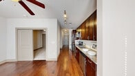 This single-floor residence offers a thoughtfully designed layout that balances functionality and style. The kitchen serves as a central highlight, showcasing rich dark mahogany cabinetry with brushed nickel hardware, light granite countertops, and a classic white subway tile backsplash. A full suite of stainless steel appliances — including a range, built-in microwave, dishwasher, and refrigerator — equips the space for everyday use. Track lighting overhead provides focused illumination throughout the kitchen.

Warm hardwood flooring extends through the main living and kitchen areas, lending a cohesive and inviting aesthetic. A hallway connects the kitchen to the rest of the unit, finished with flush-mount ceiling lighting and leading to a paneled entry door.

The bedroom features soft wall-to-wall carpeting, a ceiling fan, and a set of double doors opening to a closet, creating a comfortable and functional retreat. The bathroom maintains design consistency with dark cabinetry, granite countertops, a framed vanity mirror, and tile flooring. Upper storage cabinets provide added utility. The overall palette of neutral walls paired with warm wood tones creates a clean, modern ambiance throughout the space.