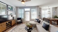 Located at 3030 Barrow Rd. in Charlotte, NC, this single-floor residence offers a thoughtfully designed layout with a contemporary aesthetic throughout. The open living area is bathed in natural light from large windows dressed with sheer curtains and wood blinds, creating a bright and airy atmosphere. Ceiling fans are featured in multiple rooms, adding both function and style.

The kitchen is outfitted with rich dark wood cabinetry, white subway tile backsplash, light countertops, and a full suite of stainless steel appliances including a range, over-the-range microwave, dishwasher, and side-by-side refrigerator. Light hardwood-style flooring flows through the kitchen and main living spaces.

The dining area is highlighted by an elegant geometric pendant light above a rustic wood table, flanked by large windows that invite natural light. The living room features a neutral color palette with a large sectional sofa and direct access to an exterior door.

The primary bedroom offers a serene retreat with plush carpeting, ceiling fan, and decorative pendant lighting. A second bedroom features a bold navy accent wall, ceiling fan, and large windows. Both bathrooms include dark wood vanities with light countertops; the primary bath features a double vanity and walk-in closet. A dedicated in-unit laundry area with washer and dryer completes this well-equipped residence.
