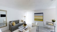 This single-floor space offers a thoughtfully designed interior that blends modern aesthetics with a welcoming, light-filled atmosphere. The living area serves as the centerpiece of the space, showcasing a clean white color palette complemented by striking yellow accents that bring energy and warmth to the room. Large sheer-draped windows allow abundant natural light to flood the interior, creating an airy, open ambiance throughout.

The living area is furnished with a classic gray sofa accented with patterned throw pillows, paired with sleek white armchairs arranged around a glass-top coffee table — a combination that balances comfort with contemporary style. A bold, large-format abstract artwork anchors one wall, featuring a dramatic composition of yellow, gray, and black tones that ties the room's color story together beautifully.

Light tile flooring runs throughout, contributing to the spacious and seamless feel of the interior. A textured white area rug grounds the seating arrangement, adding warmth underfoot. The textured ceiling adds subtle architectural character while maintaining the overall brightness of the space. A sleek floor lamp provides additional ambient lighting, rounding out this well-curated, modern living environment.