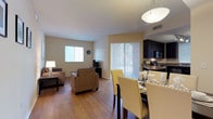 This single-floor residence offers a thoughtfully designed open-concept layout that seamlessly connects the living, dining, and kitchen areas. The living room features warm hardwood-style flooring, neutral-toned walls, and generous natural light streaming through blinds-covered windows, complemented by comfortable seating and tasteful wall art. A sliding glass door opens to an outdoor area, enhancing the sense of openness.

The dining area accommodates a full-sized table with upholstered seating beneath a stylish pendant light, flowing naturally into the kitchen. The kitchen is outfitted with rich dark cabinetry, granite-style countertops, stainless steel appliances including a dishwasher, and ample storage throughout.

The residence includes multiple bedrooms, each carpeted for comfort and filled with natural light through sizable windows. The primary bedroom features a ceiling fan, a walk-in closet, and generous space for furnishings. A secondary bedroom comfortably accommodates twin beds, also with a ceiling fan.

The bathrooms are finished with tile flooring, dark vanity cabinetry, granite-style countertops, and large mirrors. One bathroom includes a full tub-shower combination with tile surround. Throughout, the warm, neutral color palette and consistent design elements create a cohesive and comfortable living environment.