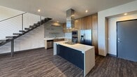 This contemporary two-story residence offers 2,310 square feet of thoughtfully designed living space across two floors, each approximately 1,130–1,180 square feet. The main floor features an open-concept kitchen and living area with dark hardwood-style flooring throughout. The kitchen is equipped with warm wood cabinetry, white quartz countertops, stainless steel appliances including a double wall oven, built-in microwave, French door refrigerator, and a tile mosaic backsplash. A sleek floating staircase with a cable-wire railing system connects the two floors. The upper level is carpeted and houses four bedrooms, including a spacious 360 sq ft primary suite with a large walk-in closet featuring built-in shelving and hanging rods. The primary bathroom is a standout, showcasing floor-to-ceiling dark slate tile, a rain showerhead, recessed wall niches, and a soaking tub enclosed by a glass partition. A dedicated laundry room with side-by-side washer and dryer and overhead wire shelving adds convenience. Bedrooms feature recessed lighting and some include sliding glass doors opening to a balcony with expansive views of the surrounding neighborhood and distant mountain ranges.