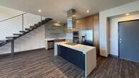 This contemporary two-story residence offers 2,310 square feet of thoughtfully designed living space across two floors, each approximately 1,130–1,180 square feet. The main floor features an open-concept kitchen and living area with dark hardwood-style flooring throughout. The kitchen is equipped with warm wood cabinetry, white quartz countertops, stainless steel appliances including a double wall oven, built-in microwave, French door refrigerator, and a tile mosaic backsplash. A sleek floating staircase with a cable-wire railing system connects the two floors. The upper level is carpeted and houses four bedrooms, including a spacious 360 sq ft primary suite with a large walk-in closet featuring built-in shelving and hanging rods. The primary bathroom is a standout, showcasing floor-to-ceiling dark slate tile, a rain showerhead, recessed wall niches, and a soaking tub enclosed by a glass partition. A dedicated laundry room with side-by-side washer and dryer and overhead wire shelving adds convenience. Bedrooms feature recessed lighting and some include sliding glass doors opening to a balcony with expansive views of the surrounding neighborhood and distant mountain ranges.