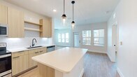 This single-story home features a thoughtfully designed open-concept layout that maximizes its well-proportioned floor plan. The combined kitchen and living area serves as the heart of the space, where a large central island with a crisp white quartz countertop anchors the kitchen. Light wood cabinetry, a subway tile backsplash, stainless steel appliances, and a matte black sink fixture contribute to the modern aesthetic. Two pendant lights with glass jar shades hang above the island, providing both task lighting and visual interest. The adjacent living area receives generous natural light through multiple windows and a glass-paneled exterior door, offering outdoor views.

Light hardwood flooring flows consistently throughout the home, complementing the neutral wall tones. A central hallway connects the three bedrooms, each featuring windows with blinds that allow for natural light and outdoor views. One bedroom includes a ceiling fan, while all rooms maintain a clean, minimalist character. The two bathrooms feature light wood vanities, white countertops, large framed mirrors with matte black trim, and tiled tub-shower combinations. A dedicated laundry room houses a full-size washer and dryer with overhead shelving, adding practical convenience to the home.