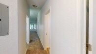 This single-story space is thoughtfully laid out, connecting its rooms through a carpeted hallway lined with textured walls and flush-mount ceiling lighting. The hallway leads toward a naturally lit area at its end, with doors branching off to various rooms along the way.

The kitchen is a functional highlight, showcasing white shaker-style cabinetry, light stone-look countertops, and a full suite of stainless steel appliances including a refrigerator, electric range with over-the-range microwave, and dishwasher. Wood-look plank flooring grounds the space with a warm, clean aesthetic.

The living and dining areas feature plush carpeting underfoot. The dining area is distinguished by a vaulted ceiling and an elegant chandelier, lending a sense of height and refinement. A window provides natural light and views of surrounding greenery.

The bedrooms are carpeted and well-proportioned, each featuring windows that allow natural light and outdoor views of mature trees. One bedroom includes a closet door, adding practical storage.

The bathroom features wood-look plank flooring, white cabinetry with stone-look countertops, and clean, bright finishes throughout. The overall ambiance of the space is neutral, bright, and move-in ready.
