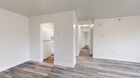 Located at 6 Bleecker Terr in Albany, NY, this 2-bedroom unit offers a clean, modern aesthetic across a thoughtfully arranged single-floor layout. The living area is bright and open, featuring light hardwood-style flooring and a large window that frames views of surrounding trees, creating an airy, welcoming atmosphere. The kitchen is efficiently designed with crisp white cabinetry, white appliances including a refrigerator and electric range, a single-basin sink, and matching hardwood-style flooring that extends from the main living areas. A central hallway connects the living spaces to the bedrooms, both of which are carpeted and feature windows with natural views. The primary bedroom is generously sized and includes access to a closet and an adjacent bathroom. The second bedroom is comfortably scaled and equally bright. A dedicated closet space with built-in shelving and a laundry hookup adds practical utility to the unit. Throughout, the space is finished with clean white walls, modern black-framed windows, and baseboard heating, contributing to a fresh, move-in-ready feel that balances functionality with understated style.