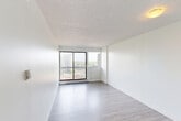 Located at 14255 Boulevard Gouin Ouest in Montréal's Pierrefonds-Roxboro neighbourhood, this well-appointed one-bedroom, one-bathroom unit offers a functional and efficiently designed layout spread across a single floor. Light wood-effect flooring runs throughout the main living areas, creating a clean and cohesive aesthetic.

The open-concept living area is bright and airy, anchored by large sliding glass doors that lead to a private balcony. The expansive windows frame elevated views of surrounding treetops and neighbouring buildings, allowing generous natural light to fill the space. A textured ceiling adds a classic architectural detail throughout.

The kitchen is set in a semi-open pass-through configuration, separated from the living and dining area by a half-wall counter, providing both defined cooking space and visual connectivity to the main room.

The bedroom is comfortably proportioned and features a built-in sliding-door closet for ample storage. A corner window admits additional natural light and continues the scenic outdoor views. Baseboard heating units are present throughout, ensuring year-round comfort.

The bathroom is finished with large-format beige stone-effect wall tiles surrounding a full soaking tub, conveying a clean and timeless aesthetic. Overall, this unit offers a practical and bright living environment in a well-situated Montréal location.