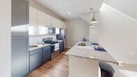 Located at 15902 White St in Charlotte, NC, this two-story home showcases a thoughtfully designed layout with modern finishes throughout. The main living area impresses with soaring vaulted ceilings and a large multi-pane window arrangement that floods the space with abundant natural light, creating an open and airy atmosphere. Hardwood-style flooring flows throughout the main living areas, complementing the home's contemporary aesthetic.

The kitchen is well-appointed with two-tone cabinetry — crisp white upper cabinets paired with slate-blue lower cabinets — granite countertops, stainless steel appliances, and a peninsula with pendant lighting overhead, making it both functional and stylish.

The upper level features an open loft space framed by sleek black cable railings, offering flexible use as a lounge, office, or play area. Ceiling fans are present in multiple rooms for added comfort. The bedrooms are carpeted and bathed in natural light through double windows with blinds, providing a warm and restful environment.

The bathroom is generously proportioned, featuring dark cabinetry with granite countertops, hardwood-style flooring, and a full tub-shower combination. Neutral tones and recessed lighting throughout the home contribute to a clean, modern, and inviting overall ambiance.