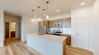 Located in Queen Creek, Arizona, this thoughtfully designed single-story residence offers a clean, modern aesthetic throughout. The open-concept kitchen and living area serves as the heart of the home, anchored by a large central island with a quartz countertop and an integrated sink, illuminated by stylish pendant lighting. Warm wood-toned cabinetry extends to the ceiling, complemented by a white subway tile backsplash and a full suite of stainless steel appliances, including a refrigerator, range, and built-in microwave. Light-toned hardwood-style flooring flows throughout the main living areas, enhancing the bright, airy atmosphere. The living room benefits from natural light through multiple windows and a sliding glass door, with a ceiling fan adding comfort. The bedroom features plush carpeting, a ceiling fan, a sunlit window, and direct access to a spacious walk-in closet outfitted with built-in shelving and hanging rods. The full bathroom includes a wood-vanity with quartz countertop, a large mirror, and a shower-tub combination. A dedicated laundry room with a full-size washer and dryer and built-in shelving adds everyday convenience to this well-appointed home.