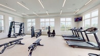 Located at 3604 Oakbrook Ln in Panama City, FL, this modern fitness center is a single-floor facility designed to support a comprehensive range of workout routines. The space is thoughtfully laid out across several interconnected zones, each dedicated to a specific type of exercise.

The main cardio and strength area is bright and expansive, featuring large windows along multiple walls that flood the space with natural light and offer pleasant views of the surrounding outdoor environment, including a pool and green landscaping. Treadmills, ellipticals, and a recumbent bike are lined along the windowed walls, while a collection of weight benches, cable machines, and multi-functional strength equipment fill the central floor space. Floor-to-ceiling mirrors amplify the sense of space and allow for proper form monitoring during workouts.

A dedicated functional training zone includes a heavy bag rack, TRX suspension trainers, kettlebells, and a rowing machine, positioned beside windows with scenic water views. A separate spin studio accommodates cycling classes, equipped with Circle spin bikes and a wall-mounted TV backed by full-length mirrors.

An additional accessory area houses stability balls, resistance bands, medicine balls, and yoga mats on a wall-mounted storage rack. Linear LED lighting throughout creates a clean, energizing ambiance, while the light-toned flooring and white walls contribute to the facility's modern, airy aesthetic.