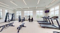 Located at 3604 Oakbrook Ln in Panama City, FL, this modern fitness center is a single-floor facility designed to support a comprehensive range of workout routines. The space is thoughtfully laid out across several interconnected zones, each dedicated to a specific type of exercise.

The main cardio and strength area is bright and expansive, featuring large windows along multiple walls that flood the space with natural light and offer pleasant views of the surrounding outdoor environment, including a pool and green landscaping. Treadmills, ellipticals, and a recumbent bike are lined along the windowed walls, while a collection of weight benches, cable machines, and multi-functional strength equipment fill the central floor space. Floor-to-ceiling mirrors amplify the sense of space and allow for proper form monitoring during workouts.

A dedicated functional training zone includes a heavy bag rack, TRX suspension trainers, kettlebells, and a rowing machine, positioned beside windows with scenic water views. A separate spin studio accommodates cycling classes, equipped with Circle spin bikes and a wall-mounted TV backed by full-length mirrors.

An additional accessory area houses stability balls, resistance bands, medicine balls, and yoga mats on a wall-mounted storage rack. Linear LED lighting throughout creates a clean, energizing ambiance, while the light-toned flooring and white walls contribute to the facility's modern, airy aesthetic.