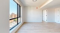 Located at 205 E 110th St in East Harlem, New York, this thoughtfully designed one-bedroom, one-bathroom residence offers a clean, contemporary aesthetic across a single floor. Light-toned hardwood flooring runs throughout, complementing bright white walls and creating a cohesive, airy atmosphere.

The kitchen showcases a modern design with two-tone cabinetry — white lower cabinets paired with natural light wood upper cabinets — set against a crisp white backsplash. Stainless steel appliances, including a freestanding range and an over-the-range microwave, add a polished, functional touch, while a deep undermount sink with a matte black faucet completes the space.

The living area benefits from large black-framed windows that flood the room with natural light and provide open city views of the surrounding East Harlem neighborhood. The bedroom continues this bright, minimalist character, featuring a floor-to-ceiling black-framed window with urban views, white walls, and light hardwood floors, along with access to a closet through clean white doors with matte black hardware.

The bathroom is a standout, finished with large-format marble-style wall tiles, a soaking tub with a matte black handheld shower fixture, and a warm wood fluted vanity topped with a white basin — a refined combination of textures and finishes that elevates the overall design.