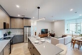 Located in the heart of Calgary's SW downtown at 8th Avenue, this well-appointed 3-bedroom, 2-bathroom unit offers a thoughtfully designed open-concept layout with modern finishes throughout. Light oak hardwood flooring flows seamlessly across the entire space, complementing the clean white walls and crisp Shaker-style interior doors with matte black hardware.

The kitchen is a standout feature, boasting two-tone cabinetry — slate grey lower cabinets paired with warm wood-grain uppers — set against a classic white subway tile backsplash. Light quartz countertops, stainless steel appliances, and a large central island with seating make it as functional as it is stylish. The kitchen opens directly into the combined dining and living area, where large windows frame urban city views and fill the space with natural light.

The living room offers generous proportions with room for comfortable seating arrangements and direct sightlines to the city skyline. Both bathrooms feature elegant marble-effect tiled tub-shower surrounds with matte black fixtures, maintaining a consistent modern aesthetic. Three well-sized bedrooms, including a spacious primary, provide ample accommodation, while multiple closets, two hallways, and an in-unit laundry room round out the highly functional floor plan.